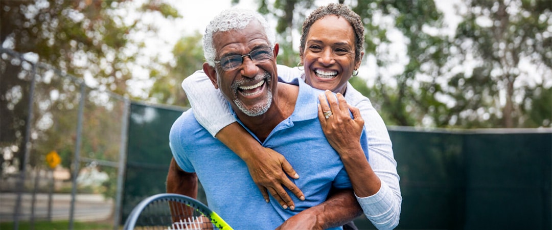 yolo-1080x450-193 An elderly couple laughing and hugging on a tennis court