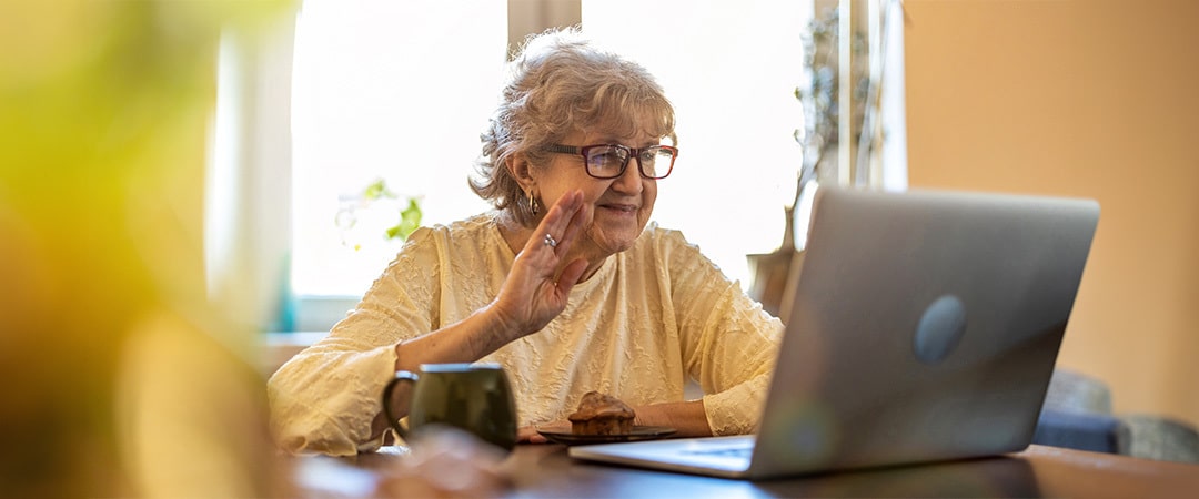 A senior woman waving to a loved one she is on a video call with on her lap top.