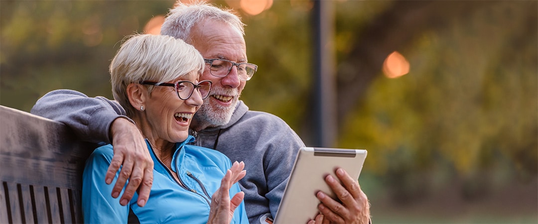 A senior couple outside looking at a tablet together on a park bench.