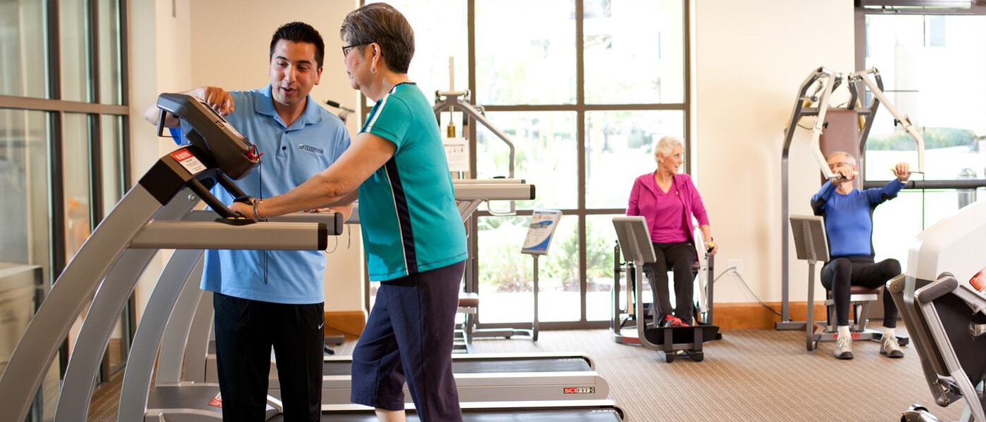 A fitness coach with an elderly woman on a treadmill